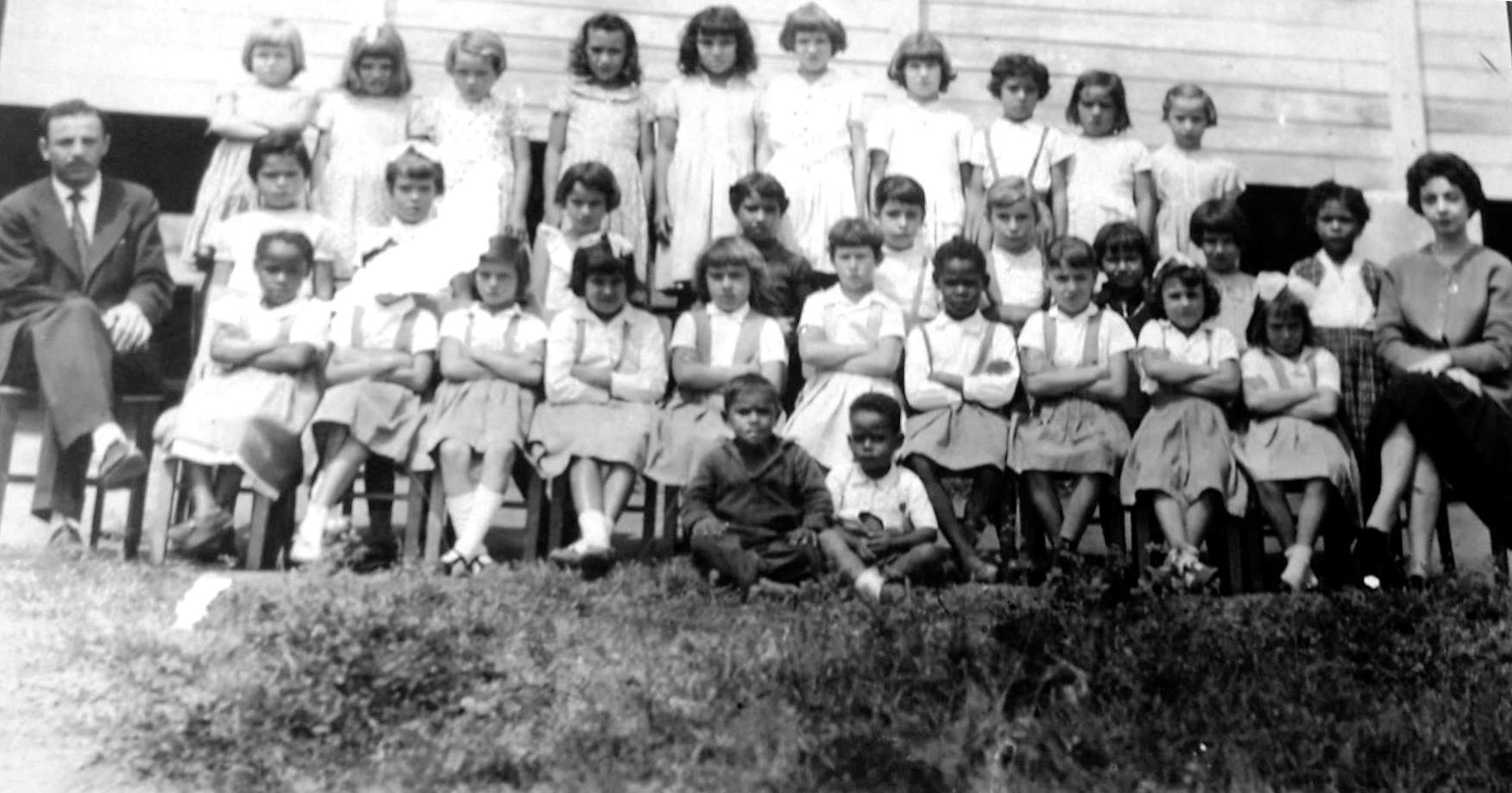 Uma das primeiras turmas das Escolas Agrupadas de São João Clímaco, com o uniforme da época, e o diretor João Bernardo, em 1957, todos à frente de um dos primeiros galpões.